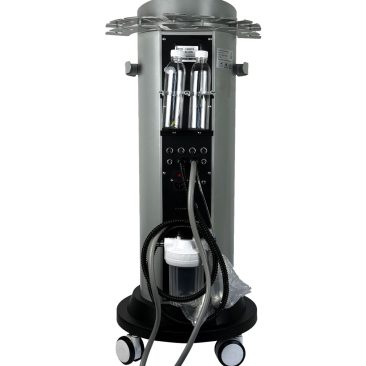 Air Essence™ Hydra Facial Therapy ESSENTIAL to cylindryczne urządzenie do hydradermabrazji na kółkach z rurkami, panelem sterowania, kablami, górną okrągłą metalową płytą z otworami oraz podstawą z przezroczystym pojemnikiem i zwiniętym wężem. Prezentowany jest tył urządzenia na którym widać gniazdo zasilające, wpięte puste przezroczyste pojemniki i 5 różnych gniazd wejściowych.