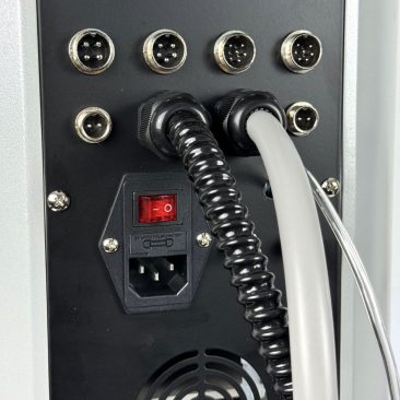 Zbliżenie tylnego panelu Air Essence™ Hydra Facial Therapy ESSENTIAL, pokazujące cztery okrągłe porty, dwa grube kable, czerwony wyłącznik zasilania, gniazdo zasilania i kratkę wentylacyjną.