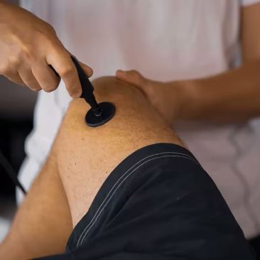 Air Essence CET RET urządzenie do terapii TECAR z wykorzystaniem fal radiowych RF stosowane do redukcji bólu i modelowania sylwetki podczas zabiegu na kolano pacjenta, widoczna głowica zabiegowa przyłożona do skóry